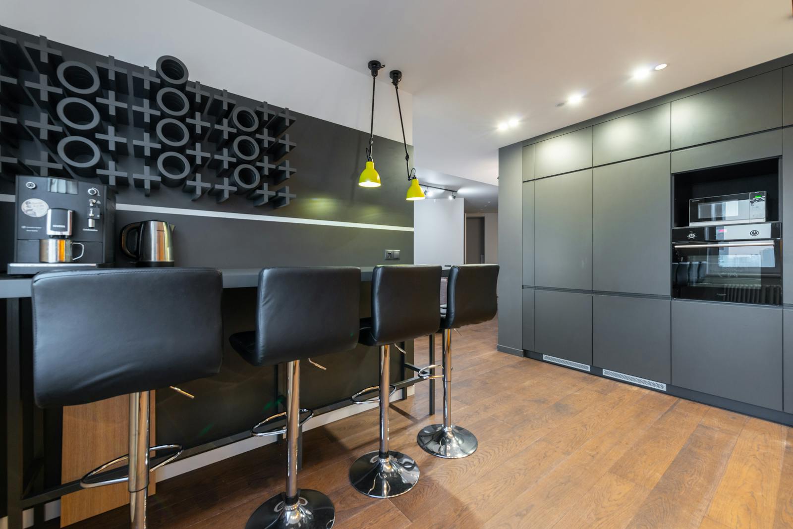 Sleek modern kitchen with bar stools, coffee machine, and stylish lighting. Ideal for interior design inspiration.